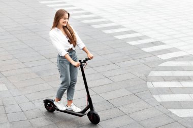 Tuğla yolda siyah scooter süren neşeli, sıradan bir kızın yüksek açılı görüntüsü, reklam veya metin için boş alan