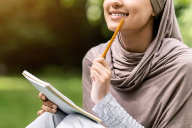 Başörtüsü içinde güzel bir kız kompozisyon yazıyor, halk parkında çalışıyor, boşluğu kopyalıyor.