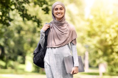 Başarılı Arap kadın, parktan yürüyen, dizüstü bilgisayarı tutan, boş alan.