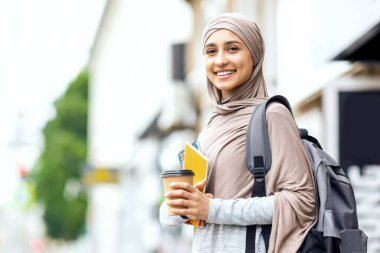 Gülümseyen Müslüman kız ders çalışmadan önce sokakta kahve içiyor.