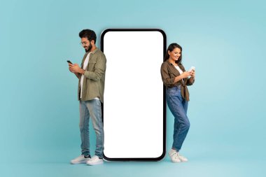 Beyaz ekranlı büyük bir telefonla poz veren zarif, genç doğu çifti, neşeli, yakışıklı Hintli adam ve akıllı telefon kullanan uzun saçlı kadın, renkli arka plan, model.