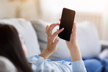 Tanımlanamayan bir kadının evde siyah ekranlı akıllı telefonu kullanırken görüntüsü, cihazla koltukta dinleniyor, boşluğu kopyalıyor.