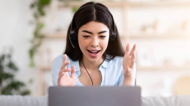 Video konferansı. Asyalı bir kızın evde dizüstü bilgisayarında web araması, oturma odasında kanepede otururken kameraya konuşması, boş yer.