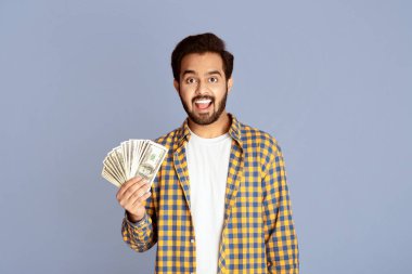 Büyük kazanç konsepti. Şaşırmış Hintli adam leylak arka planda para hayranı.