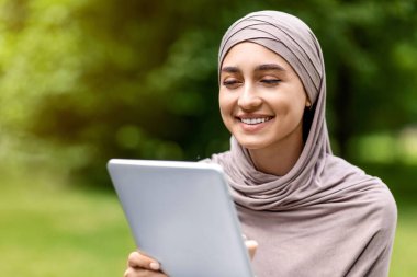 Halka açık parkta dijital tablet kullanan gülümseyen Arap kıza yakın çekim sosyal medyasını kontrol ediyor, boşluğu kopyalıyor