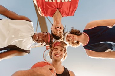 Bir grup mutlu basketbolcu kafalarını açık havada bir araya getiriyorlar. Neşeli genç sporcular oyuna hazırlanıyor. Takım çalışması spor konsepti