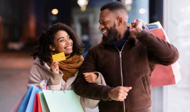Bir şeyler alalım. Gülümseyen siyah kadının portresi bankamatik kartını bir erkeğe gösteriyor, alışveriş çantalarını tutuyor, akşamları alışveriş merkezinin yakınlarında yürüyor, geçmişi bulanık.