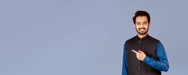 Yakışıklı genç Hintli adam gülümsüyor ve leylak arkaplanını işaret ediyor.