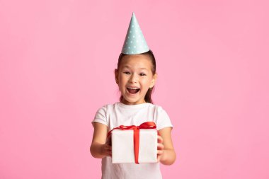 Bu senin için. Mavi parti şapkası takan, kırmızı kurdeleli neşeli Asyalı çocuk stüdyoda poz veriyor.