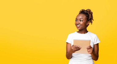 Heyecan verici bir uygulama. Dijital tabletli ilgilenen siyah kız sarı arka planda boş alana bakıyor, panorama