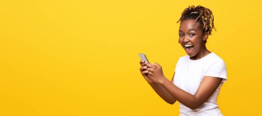 Sarı arka planda cep telefonu kullanan heyecanlı siyahi kadın, yeni bir uygulama aldı, boşluğu kopyaladı