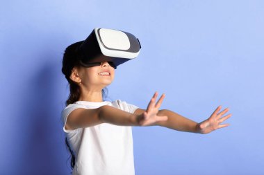 Siber uzay kavramı. VR kaskı takan mutlu Asyalı çocuk sanal gerçeklik yaşıyor, turkuaz stüdyo duvarı.