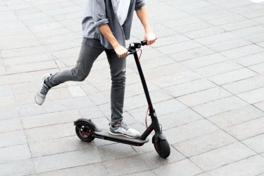 Gençlik Eğlencesi Konsepti. Uzun saçlı heyecanlı çocuğun yüksek açılı görüntüsü tuğla yolda siyah bir e-scooter sürmesi, kopyalama alanı