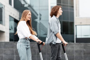 İki farklı genç açık havada scooter sürmekten hoşlanıyor. Gündüzleri modern mimari ile çevrili kentsel bir alanda dolaşırken birbirlerine gülüp kaynaşıyorlar..