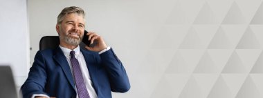 Ofiste başarılı bir yetişkin iş adamı cep telefonuyla konuşuyor, yakışıklı orta yaşlı girişimci dizüstü bilgisayarla masada oturuyor ve iş ortağıyla keyifli bir telefon görüşmesi yapıyor, boşluğu kopyalıyor.