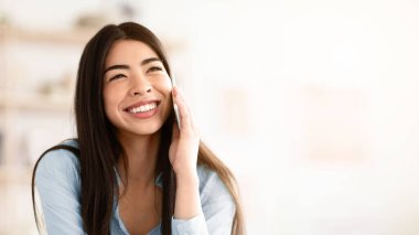 Memnun oldum. Evde cep telefonuyla konuşan neşeli Asyalı kızın yakın plan portresi, içtenlikle gülümseyen, zevk sohbeti yapan