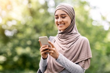 Parkta yürürken cep telefonu kullanan tesettürlü güzel Müslüman kadın, boşluğu kopyala