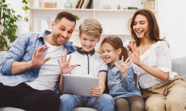 Aile dijital tabletle video görüşmesi yapıyor ve evdeki koltukta oturup selam veriyor. Uzaktan iletişim. Seçici Odaklanma