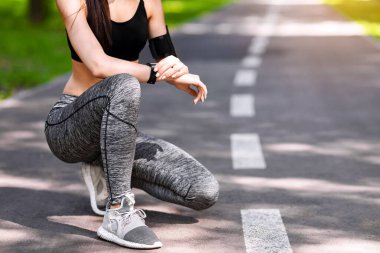 Şehir parkında koşmadan önce zamanlayıcı ayarları için akıllı saati kullanan tanınmayan sporcu kadın, boş alanlı kırpılmış resim