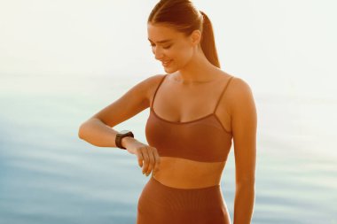 Elimizdeki akıllı cihaz. Sportif kızın portresi aktivite takip cihazını kontrol ediyor, eline bakıyor, güneş parlıyor.