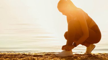 Meydan okuma kavramı. Odaklanmış kız eğitime hazırlanıyor, ayakkabılarını deniz kenarına bağlıyor, panorama, pankart