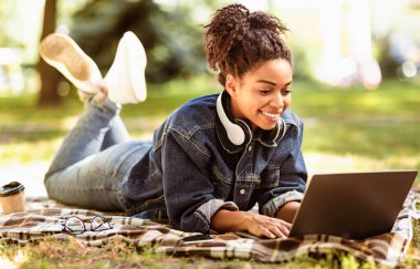 Diz üstü bilgisayarda çalışan Afrikalı Serbest Kadın dışarıda ekose üzerinde yatıyor. Uzak Görev Konsepti