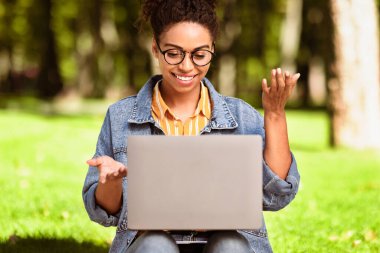 Laptop kullanan Afrikalı Amerikalı Öğrenci Kadın Yeşil Park 'ta otururken internetten öğrenme videosu çekiyor. İnternet Eğitim, E-Öğrenme ve Uzaktan Öğretim Konsepti. Seçici Odaklanma