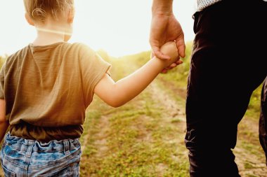Baba sevgisi kavramı. Gün batımında küçük bir çocuğun elini tutan bir ebeveynin arka görüntüsü.