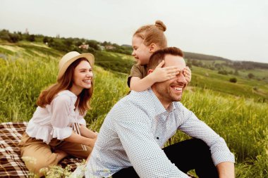 Birlikte mutluyuz. Parkta babasının gözlerini kapayan, dışarıda ona sürpriz yapan, annesine bakan genç bir kız.