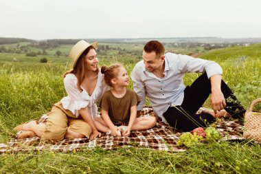 Sevgi dolu ve sevimli çocuklu bir aile hafta sonunu çayırda piknik yaparak geçirir. Birbirlerine bakarlar.