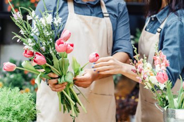 Erkek ve kadın çiçekçiler çiçekçide kompozisyona odaklandılar. Küçük işletme sahipleri, koruyucu maskeli ve önlüklü kadın ve erkek müşteriler için kovid 19 karantinası sırasında buket yaparlar.