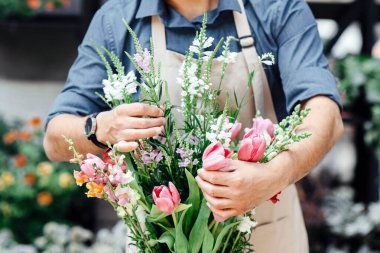 Çiçekçi taze çiçek buketi kompozisyonu yapıyor. Milenyum küçük işletme sahibi, koruyucu maskeli tasarımcı ve önlüklü müşteri için fabrika stüdyosundaki sosyal mesafe, kopyalama alanı
