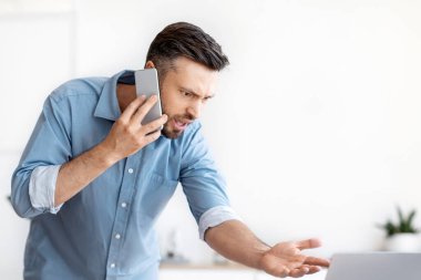 İşteki sorunlar. Sinirli iş adamı cep telefonuyla konuşuyor, dizüstü bilgisayar programında sorunları var, müşteri desteği ile konuşuyor, bilgisayar ekranına bakan memnun olmayan bir adam...