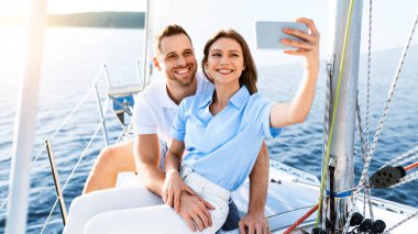 Yelkenli Yat 'ta Mutlu Eşler Tatil Yapıyor Selfie Güvertede oturmuş, Denizde Yelken Açan Telefonu kullanarak. Seçici Odaklanma