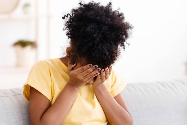 Gençlik bunalımı. Üzgün Afrikalı kız, yüzünü kapatarak ağlıyor. Evde, koltukta oturuyor..