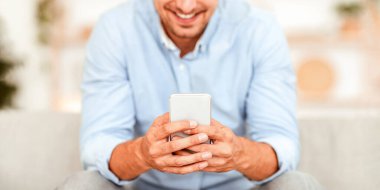 Evdeki kanepede oturan, akıllı telefonunu kullanan tanınmayan bir adamın yakın plan fotoğrafı.