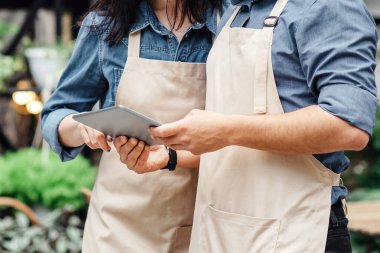 Bitki, modern uygulama, satış, yaşam tarzı ve mağaza. Önlüklü ve koruyucu maskeli meşgul erkek ve kadın dijital tablet ve blog kullanıyor ve çiçekçi dükkanının yakınında reklam veya pazarlama stüdyosu yapıyor.