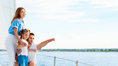 Yelkenli. Yatın üzerinde durup açık deniz sularını gösteren mutlu bir aile kucaklaşması. Anne-baba ve kızı yelkenlide birlikte hafta sonunun tadını çıkarıyorlar. Panorama, Boşluğu Kopyala
