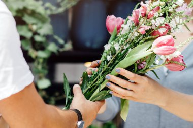Karantina ve sosyal uzaklık süresince hediye ve hizmet için çiçekler. Önlüklü ve koruyucu maskeli genç bir erkek satıcı müşteriye fabrika dükkanının yakınındaki şirin bir buket çiçek siparişi veriyor.