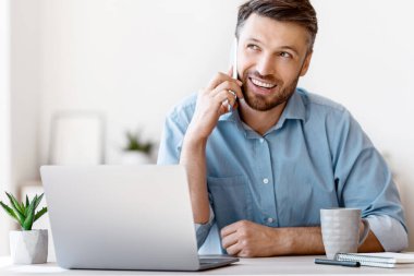 Mobil İletişim. Ofiste cep telefonuyla konuşan yakışıklı girişimci, Milenyum İşadamı dizüstü bilgisayarla masada oturuyor, keyifli telefon konuşmalarının tadını çıkarıyor, Boşluğu Kopyala