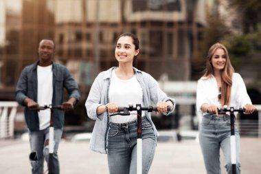 Çeşitli gençlerden oluşan bir grup, şehir merkezindeki hareketli bir sokak boyunca keyifli bir şekilde scooter kullanıyor. Dost canlısı atmosfer, arkadaşlar arasında gençlik enerjisi ve dostluk gösteriyor..