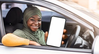 Neşeli, mutlu, tesettürlü Müslüman kadın arabasında oturuyor ve yeni ehliyetini gösteriyor, ehliyetini kutluyor, sürücü kursunu bitiriyor, sınavı geçiyor, araba alıyor, arabanın içinde oturuyor, pencereden bakıyor.