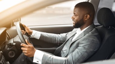 Pahalı takım elbiseli mutlu Afro-Amerikan bir adamın yan görüntüsü. Heyecanlı genç siyahi girişimci lüks arabasıyla iş toplantısına gidiyor, pencereden vuruluyor, boşluğu kopyalıyor.