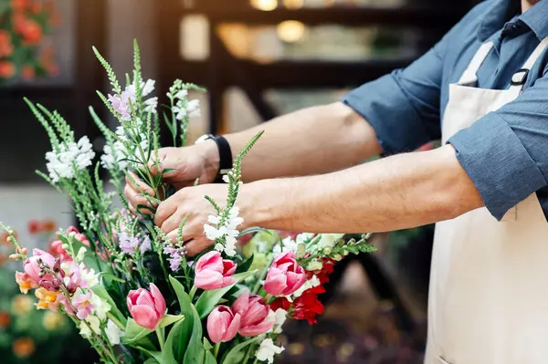 Küçük işletme, erkek çiçekçi çiçekçide kompozisyona odaklanmış. Koruyucu maskeli ve önlüklü genç tasarımcı COVID-19 kilitlenmesi sırasında müşteriye teslim etmesi için buket yapıyor.