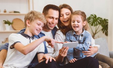 Ebeveynler ve çocuklar evdeki koltukta otururken birlikte cep telefonu kullanıyorlar. Aile Hafta Sonu Tatil Konsepti