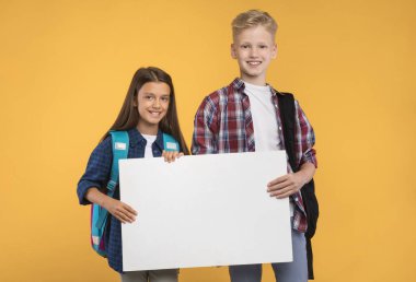 İyi teklif. İki öğrenci boş beyaz tabela tutuyor ve gülümsüyor, sarı stüdyo duvarında duruyor, boş alan.