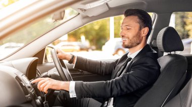 Yakışıklı bir iş adamı, araba kullanıyor, müzik açıyor, iş gezisine çıkıyor, yan manzara, fotokopi odası. Şık takım elbiseli mutlu bir adam iş toplantısına gidiyor, lüks arabasını kullanıyor, kulübeden vurulmuş.