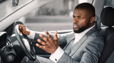 Stresli Afrikalı Amerikalı iş adamı araba sürerken bağırıyor ve el kol hareketi yapıyor, iş toplantısına gidiyor, boş yer var. Kızgın siyah adam trafiğe takıldı, geç kaldı, yandan baktı.