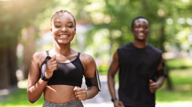 Aktif Yaşam Tarzı Konsepti. Motive olmuş Afrikalı kız erkek arkadaşıyla dışarıda koşuyor, Kameraya gülümsüyor, Seçici Odaklanma
