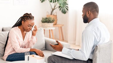 Siyahi erkek psikolog ofisinde terapi seansı sırasında ağlayan kadınla konuşuyor, depresyondaki Afrikalı Amerikalı kadınlara duygusal çöküntüden muzdarip olan kadınlara tavsiyeler veriyor,